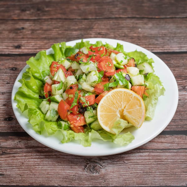 Fresh deli salad with chopped tomatoes, cucumbers, and herbs, garnished with a lemon slice.