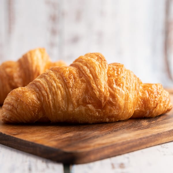 Two golden-brown, flaky croissants rest on a rustic wooden cutting board.